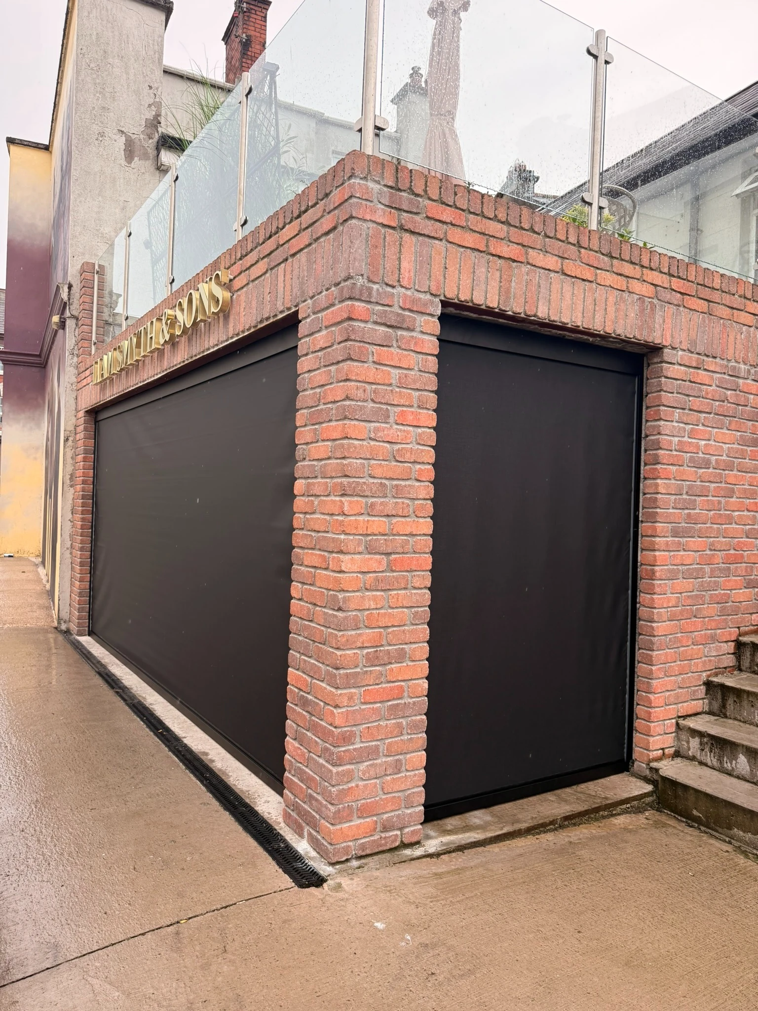 Dark guided ZIP screens surrounding a covered garden seating area during rain